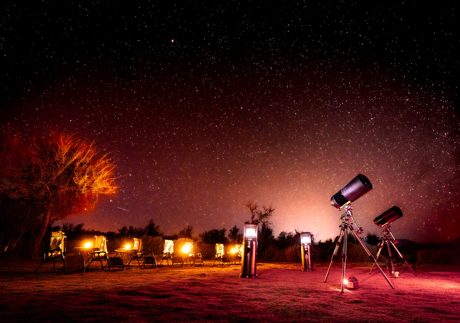 Telescopios y reposeras reclinables listos para la observación, bajo un cielo estrellado.