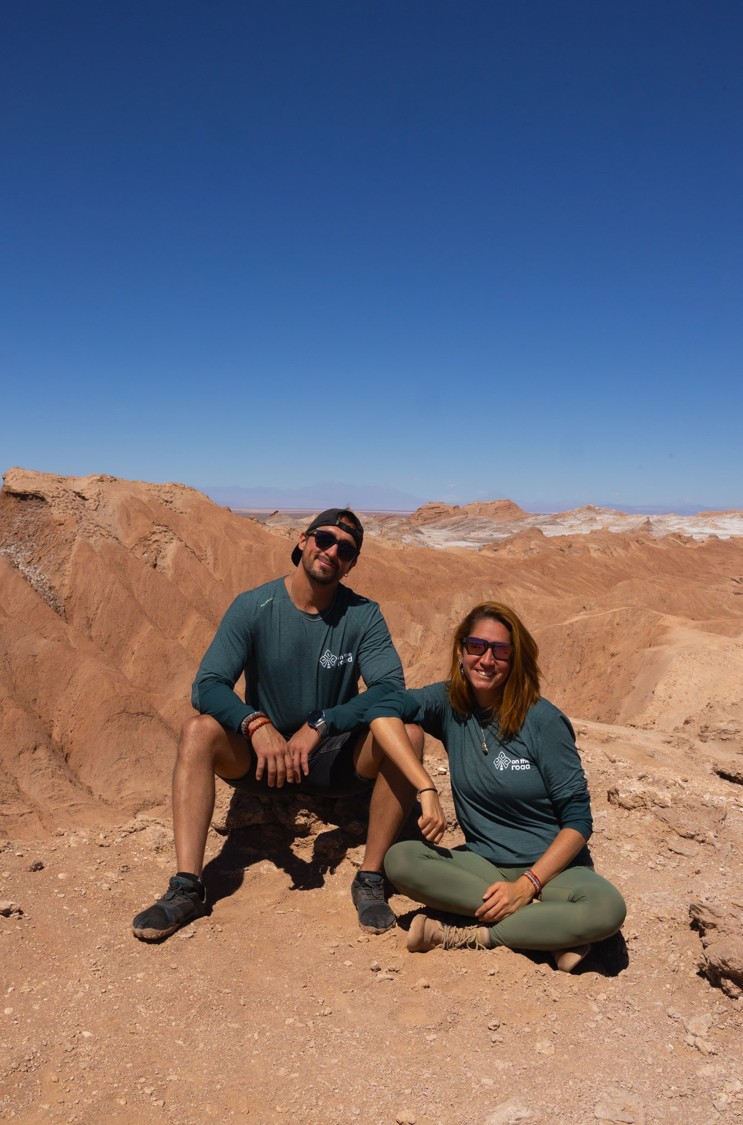 Carol e Cris sentados sobre uma rocha do Vale da Lua, sorrindo com o deserto ao fundo.
